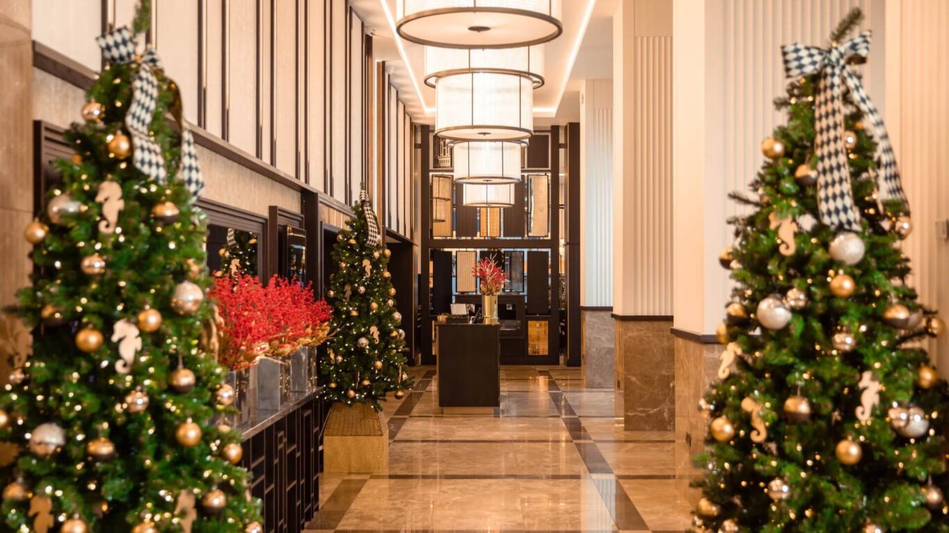 A hotel lobby decorated for Christmas, featuring evergreen trees with gold ornaments and checkered ribbons