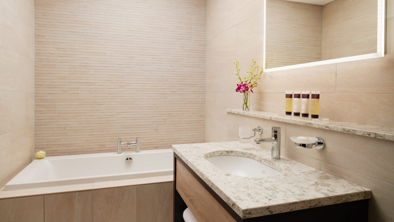 Modern bathroom with a beige tile design. Features a marble countertop with a sink, a bathtub, and a wall mirror