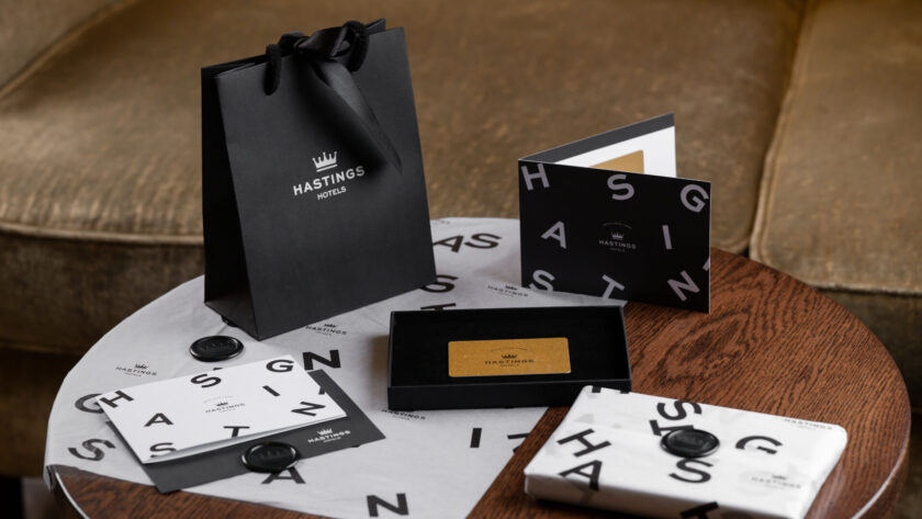 Black Hastings Hotels gift bag and packaging set on a wooden table, featuring branded cards and wrapping