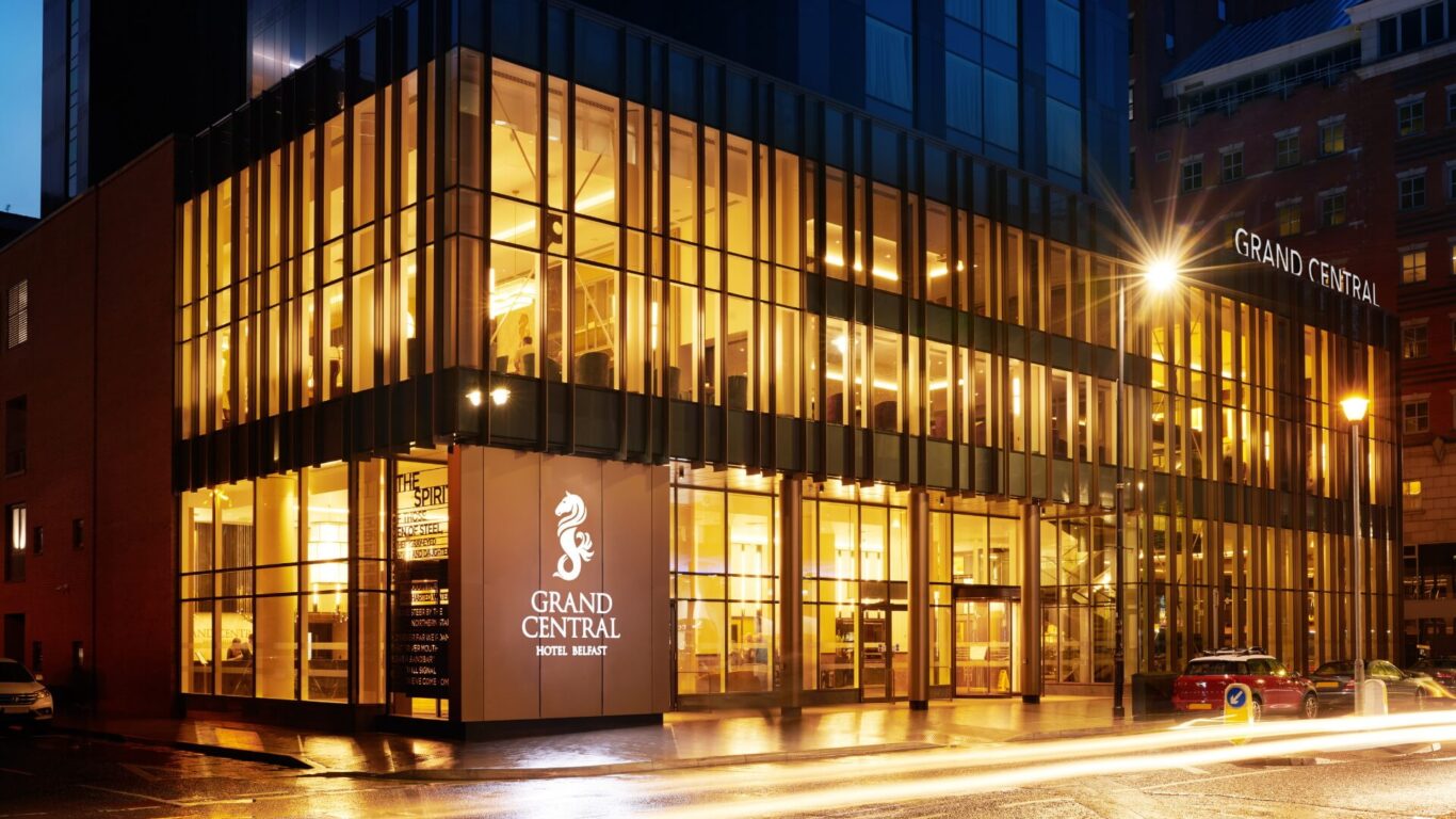 Grand Central Hotel entrance in Belfast, featuring large sleek windows and gold accents with a prominent seahorse logo