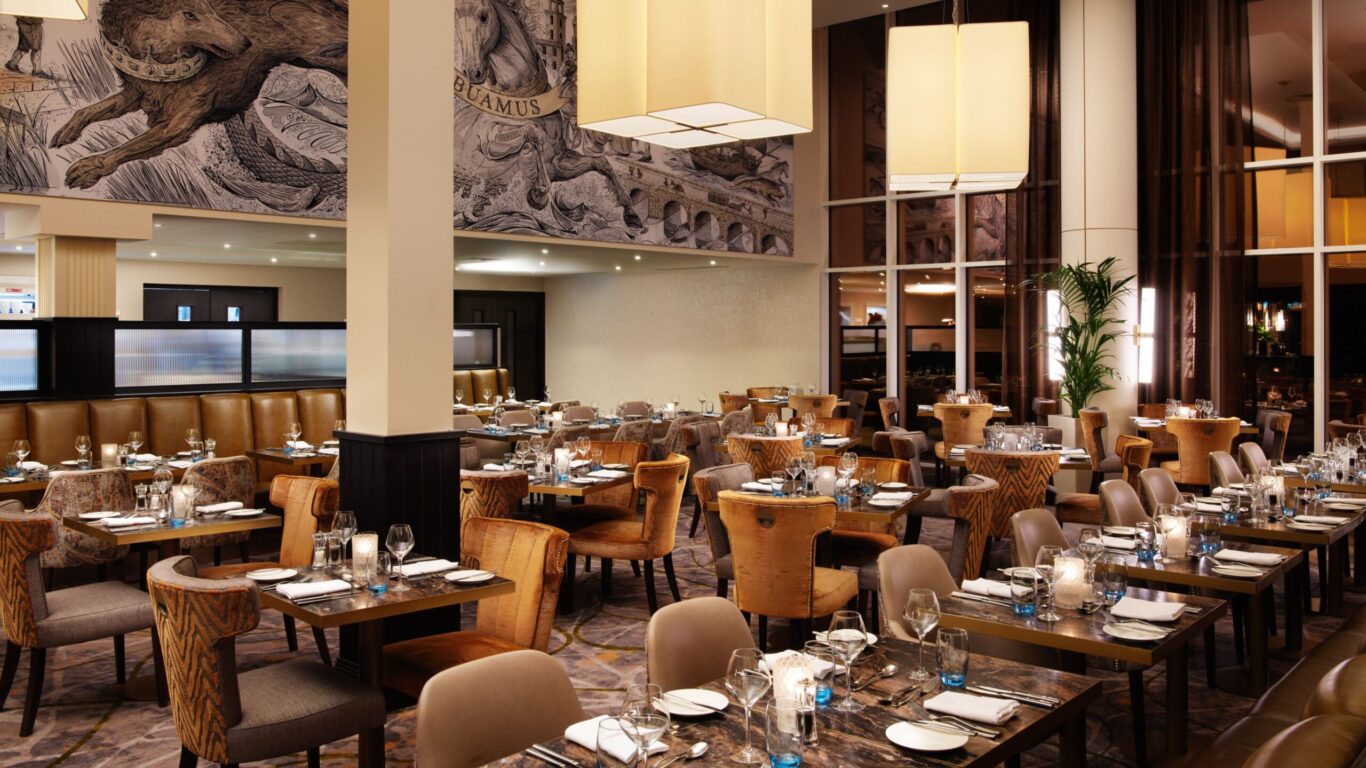Elegant restaurant interior with a warm toned interior. It features plush seating, modern chandeliers, ornate wall art, and tables set for dining.