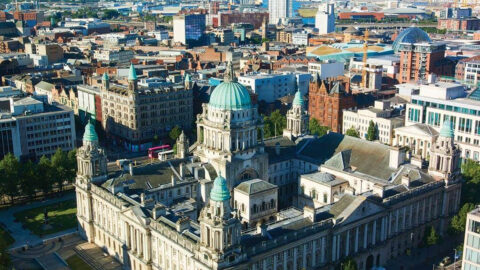 Statue of the Titanic Memorial in front of a grand historicity hall building with columns. Bare trees and a landscaped garden surround the monument.